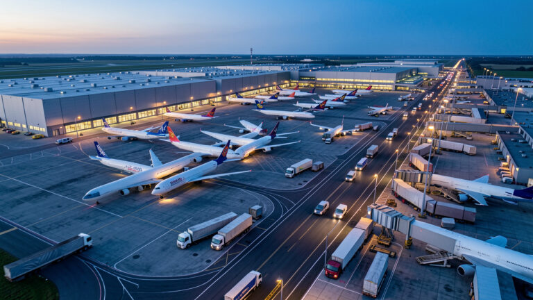 Vue aérienne d’un grand aéroport cargo britannique à l’aube, avec des avions de fret, des entrepôts logistiques éclairés et des véhicules circulant sur les voies de service.